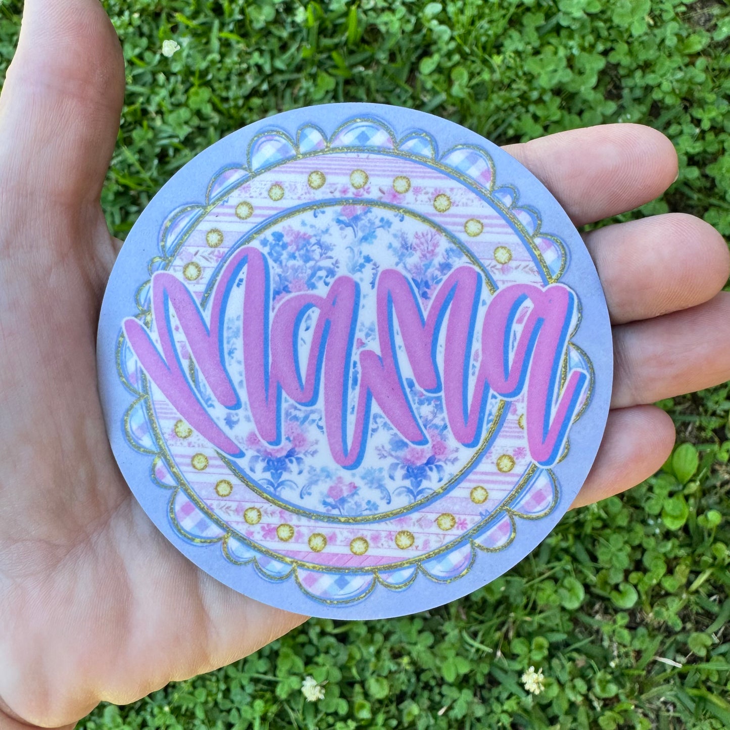 3.6 inch round circular MDF wood coaster featuring a light purple background with a large center circle showing bold pink script font reading Mama over a blue and pink vintage rose floral pattern, framed by a scalloped border with simulated gold glitter trim and pink gingham checks.