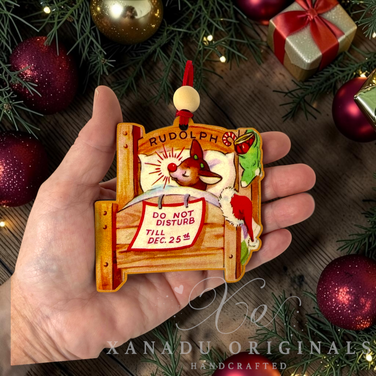 Whimsical funny reindeer holiday Christmas ornament measuring 3.42 by 3.5 inches held in a hand next to holiday tree decorations.