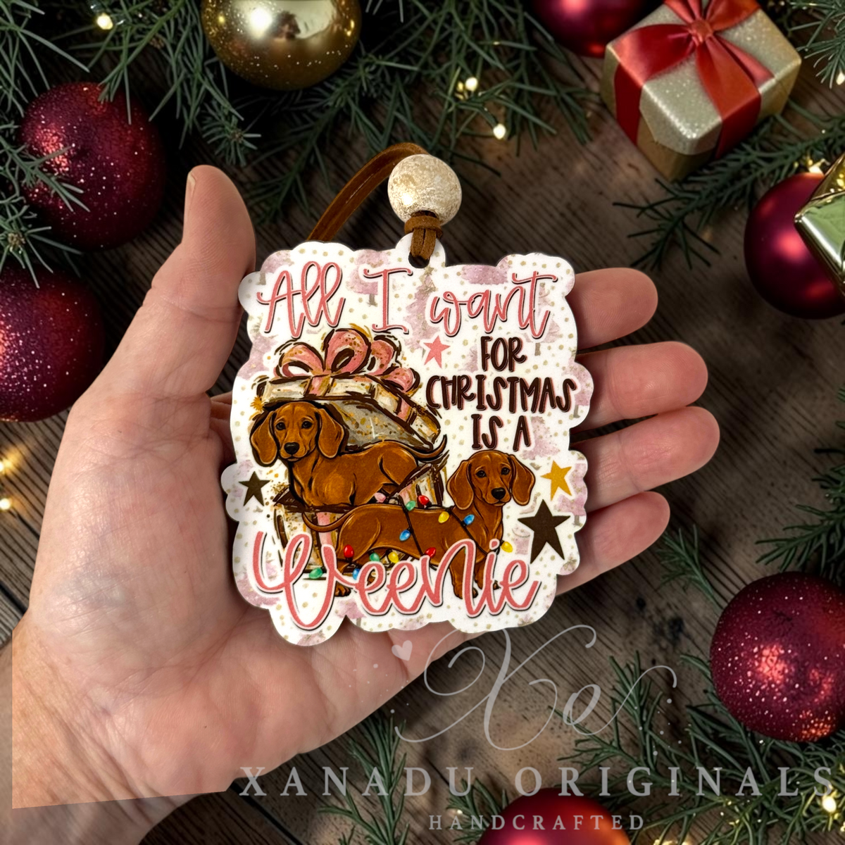 Whimsical funny dachshund dog Christmas ornament measuring 3.23 by 3.65 inches held in a hand next to holiday tree decorations.