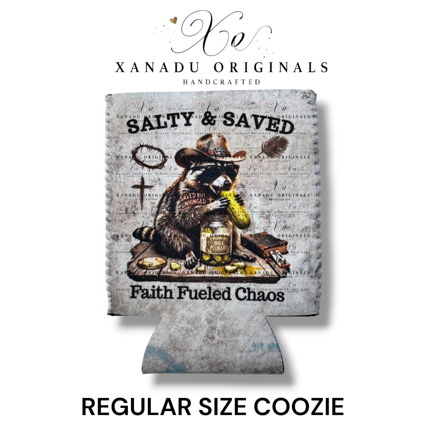 "Xanadu Originals handcrafted regular size neoprene can coozie featuring a rustic vintage illustration of a cowboy raccoon eating a dill pickle beside a cross and Bible with the text 'Salty & Saved' and 'Faith Fueled Chaos' on a gray textured background."