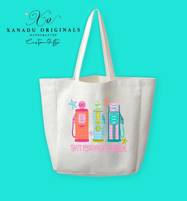 A cream-colored polyester linen tote bag featuring a retro mid-century modern graphic of three vintage gas pumps in pink, yellow, and teal with starburst details. Bright pink stylized text underneath reads "THAT'S MY BOYFRIEND'S PROBLEM."