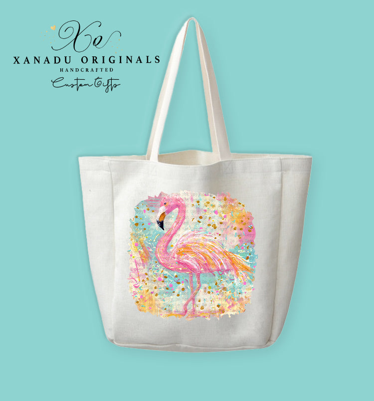 A cream-colored polyester linen tote bag featuring a textured watercolor illustration of a pink flamingo. The background is a vibrant abstract blend of yellow, blue, and pink pastel brushstrokes decorated with gold glitter speckles.