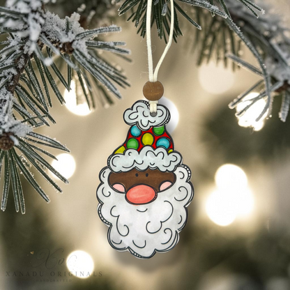 A close-up shot of a dark skin tone Santa wood ornament with a multi-colored polka dot hat hanging from a frosted pine branch against a warm, glowing holiday light backdrop.
