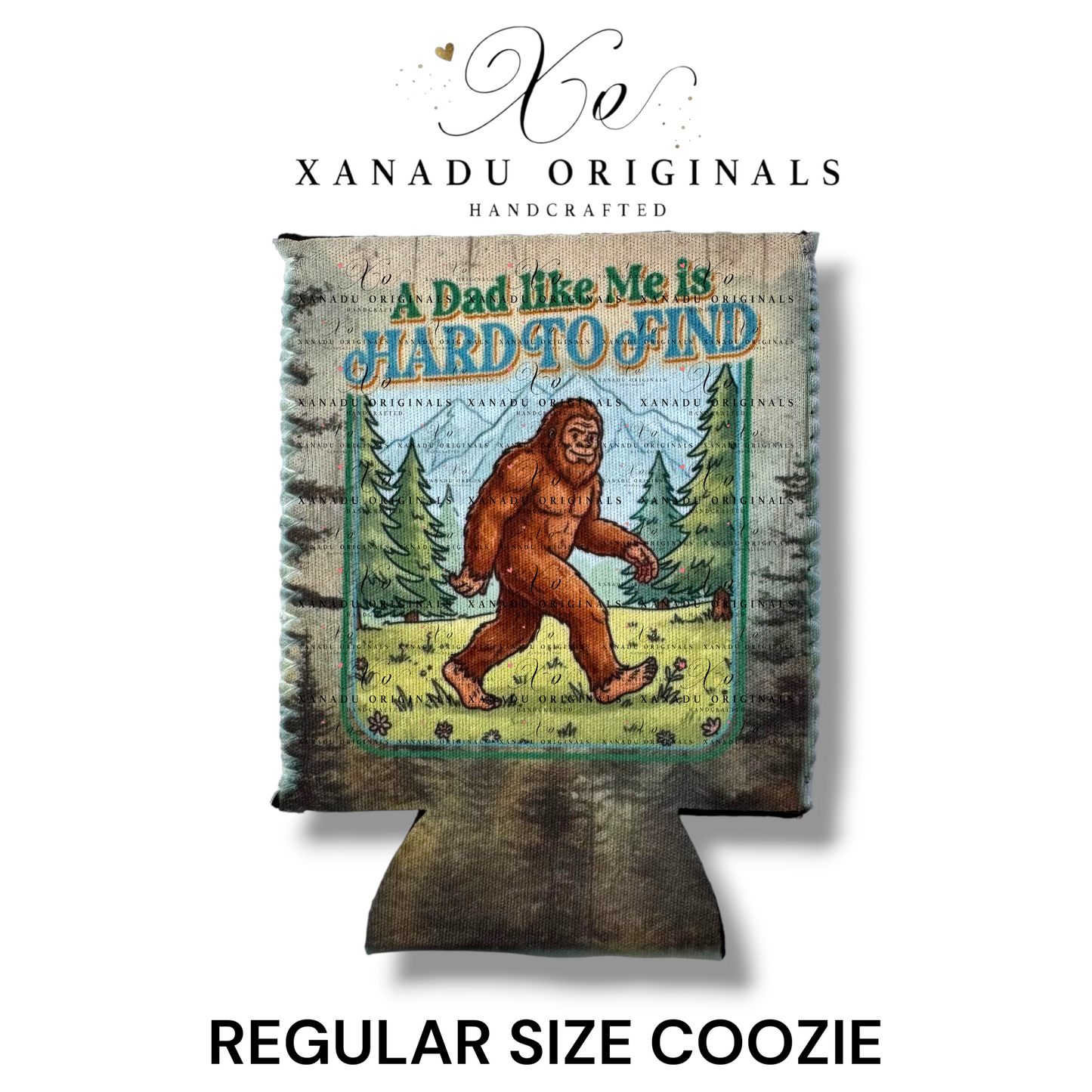 "Xanadu Originals handcrafted regular size neoprene can coozie featuring an illustration of Bigfoot walking through a pine forest with the text 'A Dad like Me is HARD TO FIND' on a rustic wood-grain texture background."