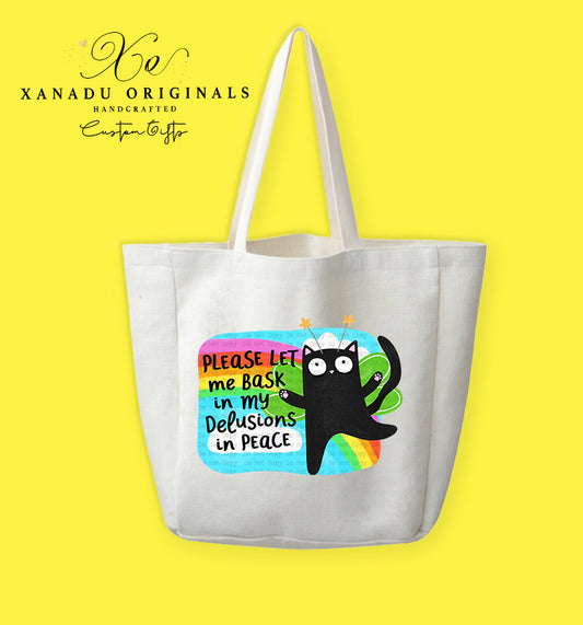 A cream-colored polyester linen tote bag featuring a cartoon illustration of a wide-eyed black cat wearing a headband with orange stars on springs. The cat is set against a bright rainbow backdrop with bold black and teal text that reads "PLEASE LET me BaSk in my Delusions in PEACE."