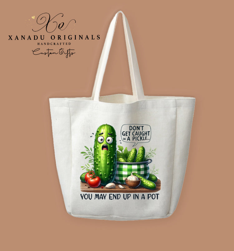 A cream-colored polyester linen tote bag featuring a funny illustration of a terrified cucumber next to a cooking pot of pickles with the text "DON'T GET CAUGHT IN A PICKLE... YOU MAY END UP IN A POT".
