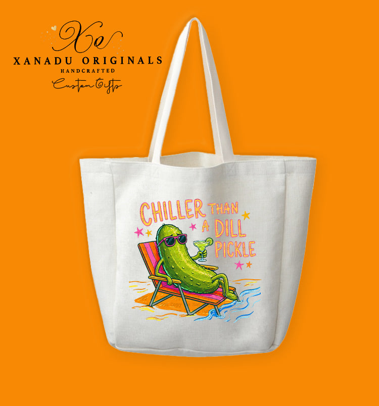 A cream-colored polyester linen tote bag featuring a colorful retro-style illustration of a green pickle wearing sunglasses on a beach lounge chair with a drink. The stylized text reads "CHILLER THAN A DILL PICKLE".