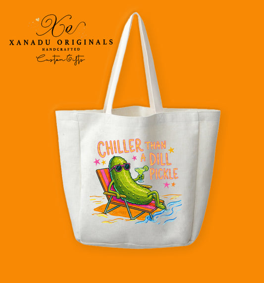 A cream-colored polyester linen tote bag featuring a colorful retro-style illustration of a green pickle wearing sunglasses on a beach lounge chair with a drink. The stylized text reads "CHILLER THAN A DILL PICKLE".
