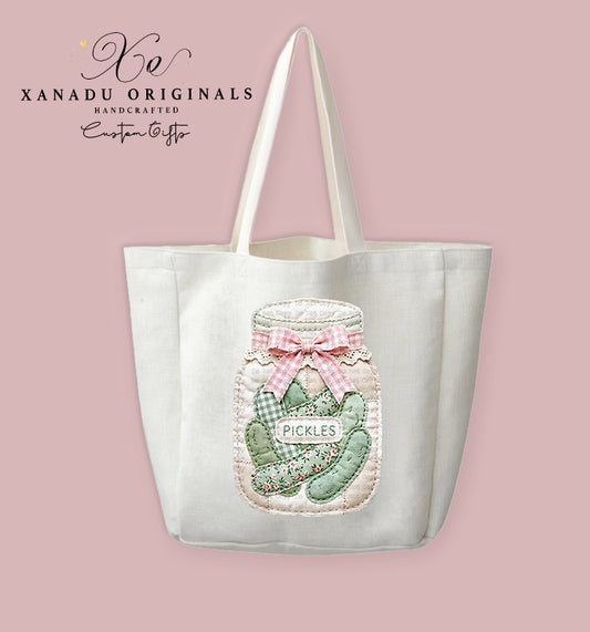 A cream-colored polyester linen tote bag featuring a digital illustration of a faux quilted patchwork mason jar filled with patterned green pickles and tied with a pink plaid bow.