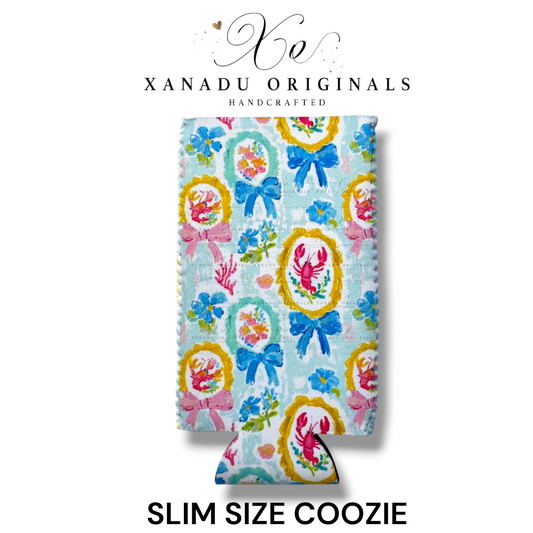 "Xanadu Originals handcrafted slim size neoprene can coozie featuring a vibrant repeating coastal pattern of pink lobsters and crabs crawfish inside ornate gold frames paired with large blue bows over a soft pastel blue background."
