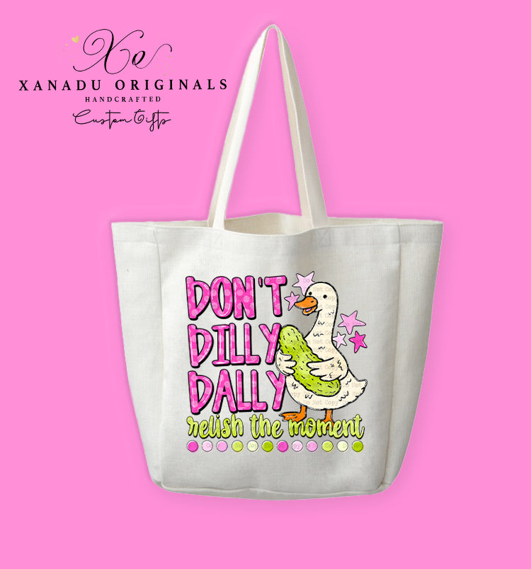 A cream-colored polyester linen tote bag featuring a cute illustration of a white duck hugging a large dill pickle next to the colorful text "DON'T DILLY DALLY relish the moment".
