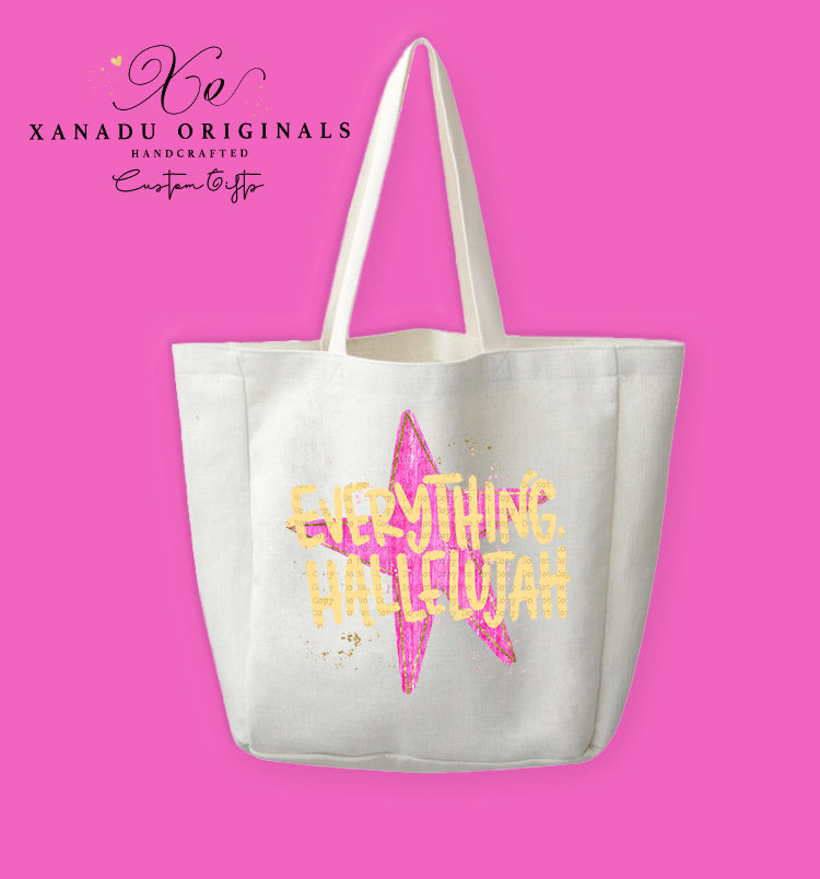 A cream-colored polyester linen tote bag featuring a large hot pink watercolor star illustration in the center. The star is decorated with fine gold glitter speckles and overlaid with bold, patterned gold text reading "EVERYTHING HALLELUJAH" in uppercase lettering.