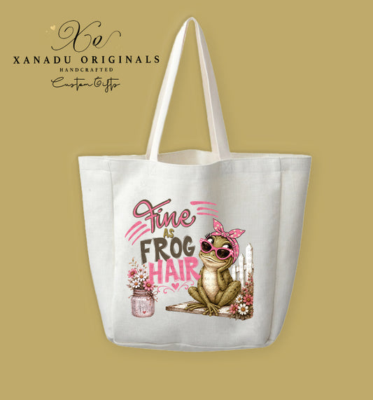 A cream-colored polyester linen tote bag featuring a watercolor illustration of a green frog in pink sunglasses and a polka-dot headband sitting by a white picket fence, alongside a pink mason jar bouquet and text reading "Fine AS FROG HAIR."
