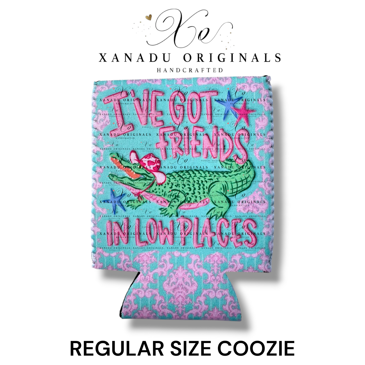 "Xanadu Originals handcrafted regular size neoprene can coozie featuring an illustrated green alligator wearing a pink cowboy hat and playing a guitar with the bold text 'I'VE GOT FRIENDS IN LOW PLACES' over a pink and blue damask background."