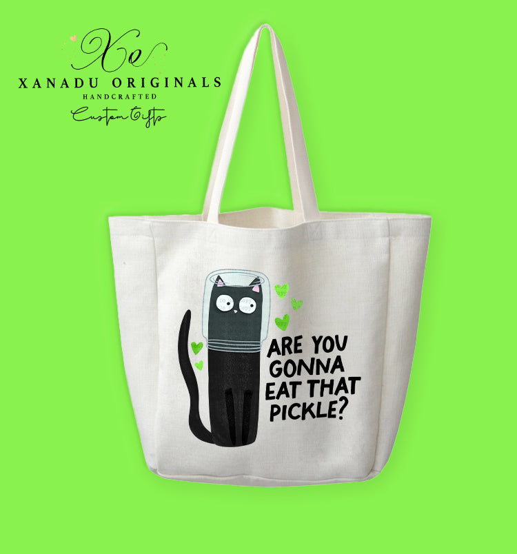 A white polyester linen tote bag featuring a whimsical graphic of a wide-eyed black cat with its head inside a pickle jar, surrounded by small green hearts, next to the text "ARE YOU GONNA EAT THAT PICKLE?".