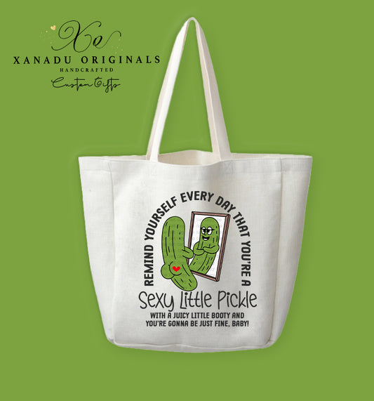 A cream-colored polyester linen tote bag featuring a funny cartoon illustration of a pickle looking in a mirror next to a motivational text overlay about being a sexy little pickle.