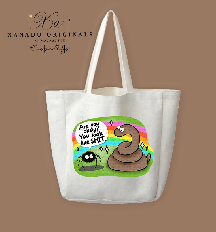 A cream-colored polyester linen tote bag featuring a vibrant, colorful cartoon illustration of a black, fuzzy spider talking to a smiling coiled brown snake. The spider has a speech bubble saying "Are you okay? You look like SHIT." against a bright rainbow backdrop with sparkling diamond stars.