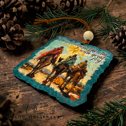 A square wooden ornament with scalloped edges, featuring an artistic depiction of three wise men and the quote 'They followed the star with great joy.' The ornament is displayed on a rustic wooden surface surrounded by pine branches and pinecones.