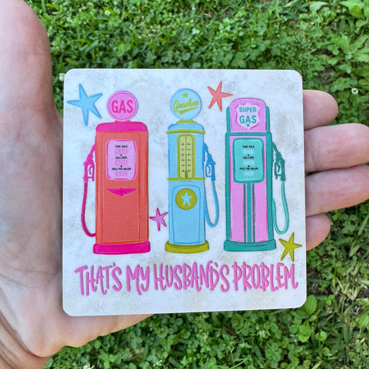 3.6 inch square MDF wood coaster with rounded corners featuring three colorful vintage retro pastel gas pumps in orange, blue, and pink with stars and text reading That's My Husband's Problem on a rustic background