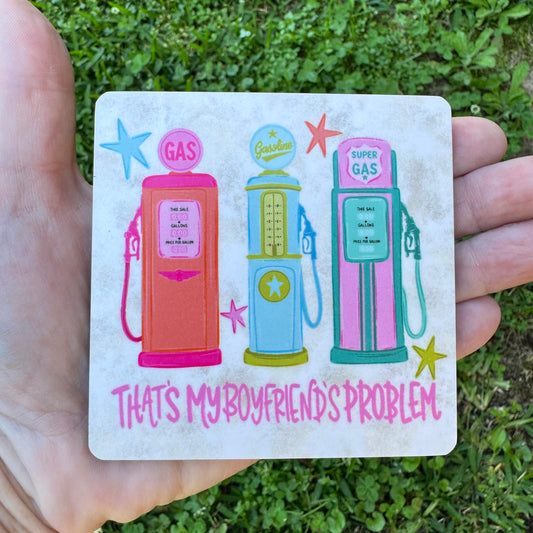 3.6 inch square MDF wood coaster with rounded corners featuring three colorful vintage retro pastel gas pumps in orange, blue, and pink with stars and text reading That's My Boyfriend's Problem on a rustic background.