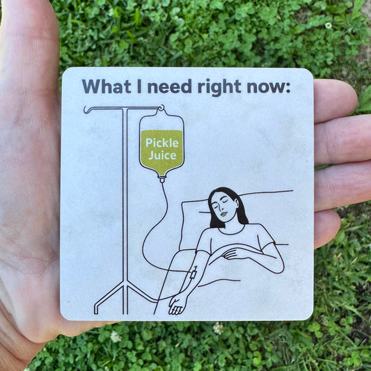 3.6 inch square MDF wood coaster with rounded corners featuring a black line art illustration of a person lying in bed hooked up to an IV pole holding a green bag labeled Pickle Juice, text above reads What I need right now.