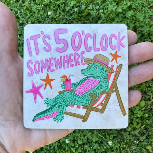 3.6 inch square MDF wood coaster with rounded corners featuring an illustration of a green alligator wearing a straw hat, lounging on a red striped beach chair holding a tropical cocktail with an umbrella, pink and orange stars, and text reading It's 5 O'Clock Somewhere.