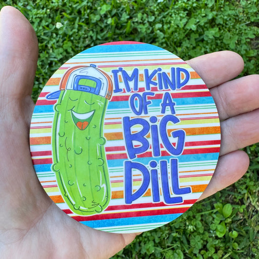 3.6 inch round circular MDF wood coaster featuring an illustration of a laughing cartoon green pickle wearing a blue and orange backward baseball cap with text reading I'm Kind of a Big Dill on a red, blue, green, and orange horizontally striped background.