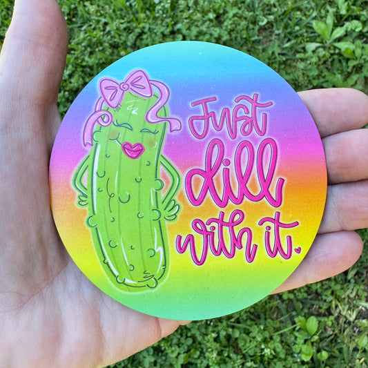 3.6 inch round circular MDF wood coaster featuring an illustration of a smiling cartoon green girl pickle wearing a pink hair bow and pink lipstick with text reading Just dill with it on a vibrant neon rainbow gradient background of blue, purple, pink, orange, yellow, and green.