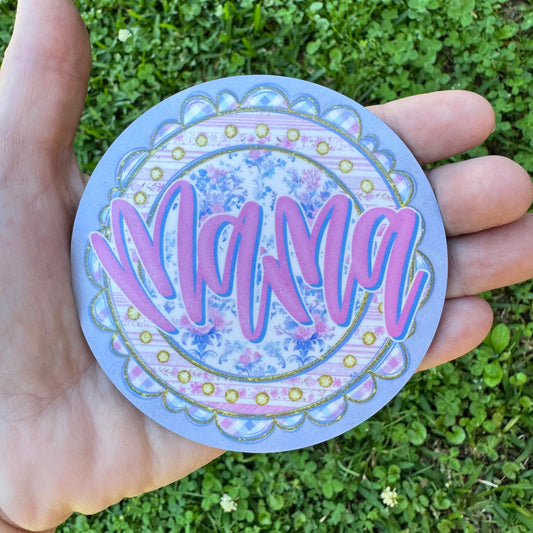 3.6 inch round circular MDF wood coaster featuring a light purple background with a large center circle showing bold pink script font reading Mama over a blue and pink vintage rose floral pattern, framed by a scalloped border with simulated gold glitter trim and pink gingham checks.