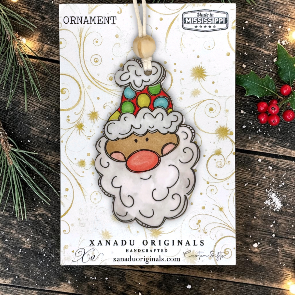 A holiday ornament display card showcasing a light skin tone Santa face wood decoration featuring a vibrant polka dot winter cap, light wood bead, and green holly leaves on a snowy dark wood surface.
