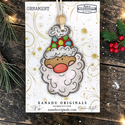 A holiday ornament display card showcasing a light skin tone Santa face wood decoration featuring a vibrant polka dot winter cap, light wood bead, and green holly leaves on a snowy dark wood surface.