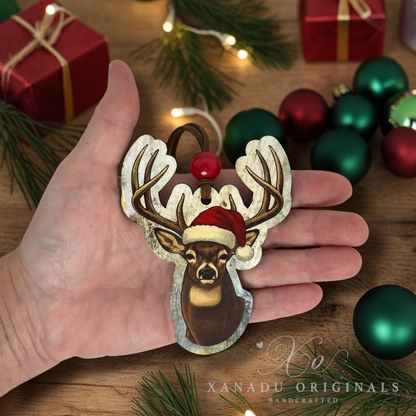 A close-up view of a hand holding the 4-inch vintage deer wood ornament, showing its size against a festive holiday background with green and red Christmas bulbs.