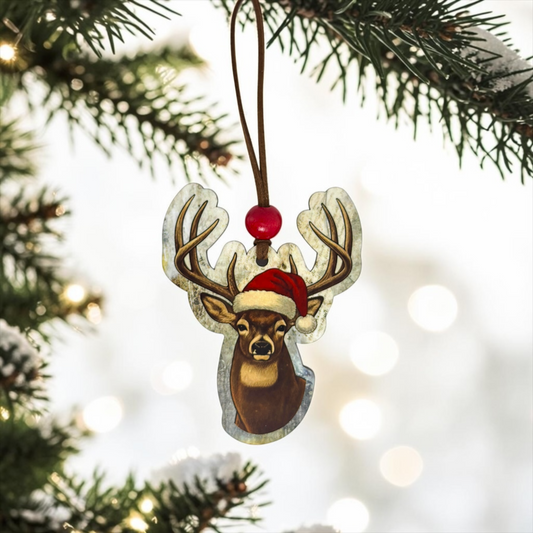  A classic buck wood ornament wearing a festive Santa hat hanging from a frosted pine branch against a soft, glowing holiday light backdrop.