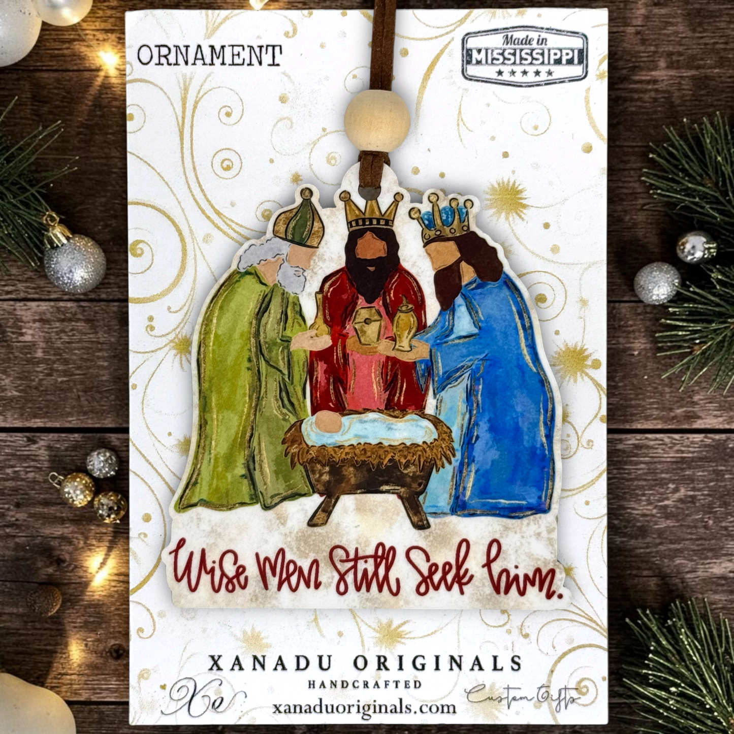 A Christmas ornament on a card featuring a nativity scene with three wise men, a crowned man in red, and a crowned man in blue around a baby in a manger. The card reads 'ORNAMENT' and 'Wise Men Still Seek Him.
