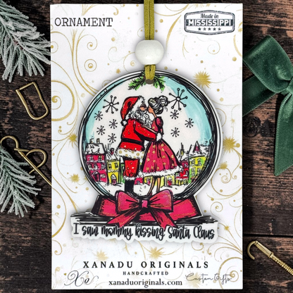 A Christmas ornament card from Xanadu Originals featuring a snow globe shaped ornament design with Santa Claus and Mrs. Claus hugging inside a snow globe, with the phrase 'I saw mommy kissing Santa Claus'.
