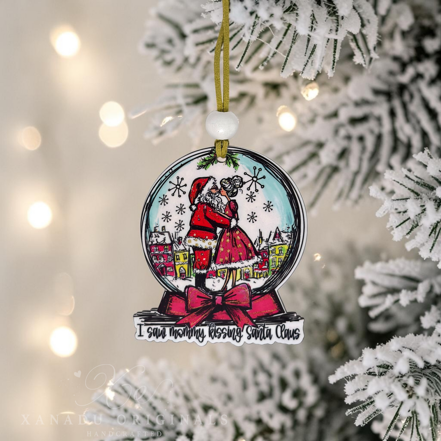 A snowglobe shaped Christmas ornament hanging from a gold ribbon on a snowy Christmas tree. The ornament features an illustrated Santa Claus and Mrs. Claus