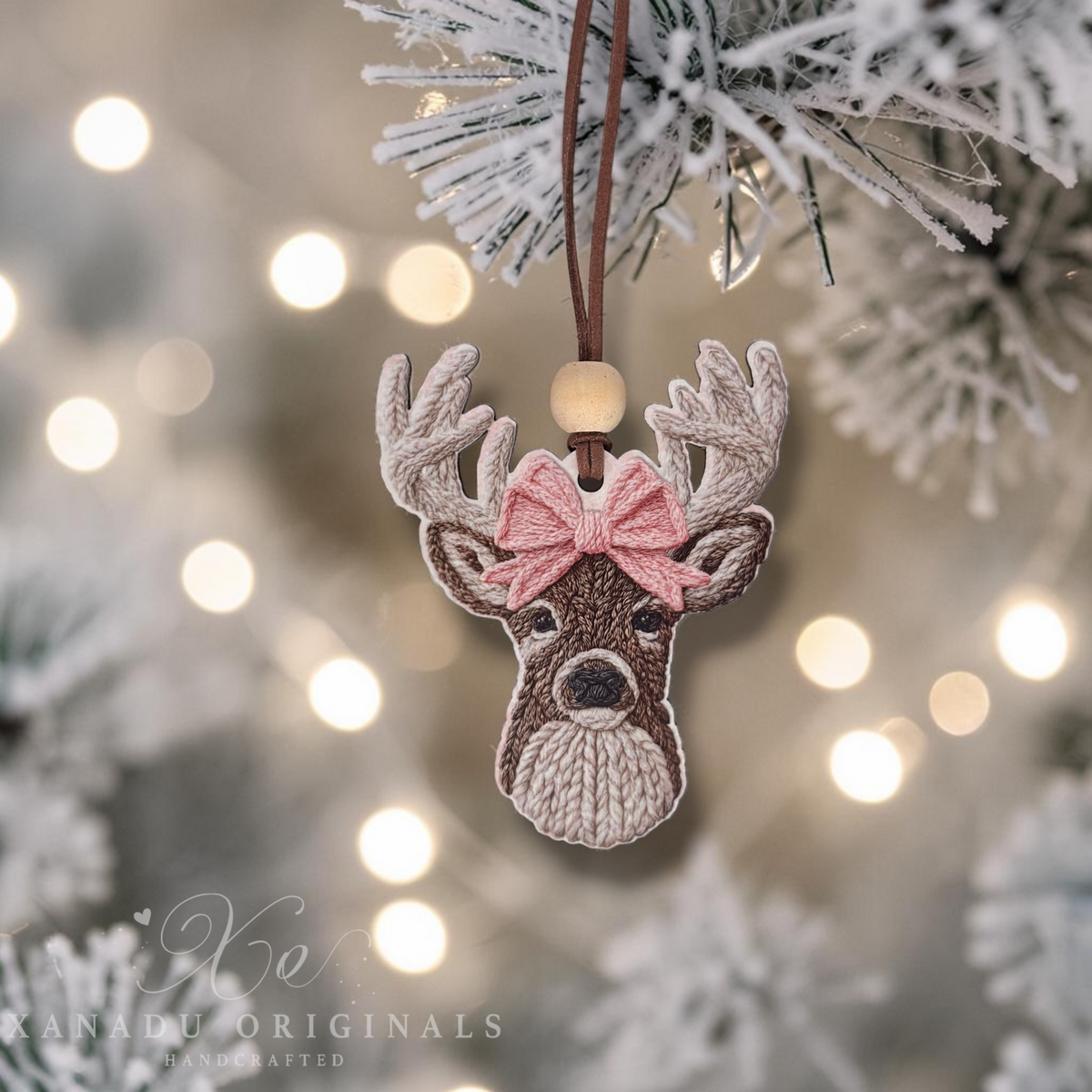 A close-up view of a cozy cable-knit style deer wood ornament hanging from a snow-flocked tree branch with a warm, glowing holiday light backdrop.