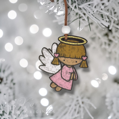 A handcrafted paper angel Christmas ornament with a brown hair halo, pink dress, and white wings, hanging from a brown string with a white bead against a blurred white Christmas tree background with bokeh lights.