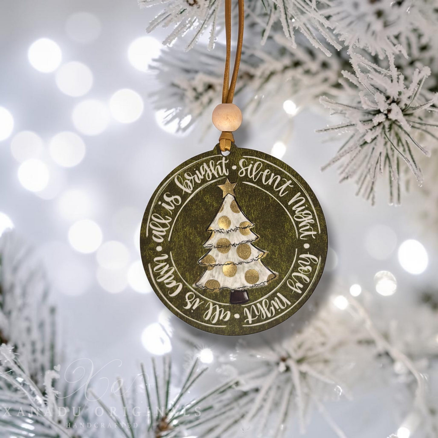 A round wooden Christmas ornament hanging from a tree branch. The ornament is dark brown with a distressed finish, featuring a hand-painted white and gold Christmas tree in the center and the words 'It is bright silent night' and 'good night all is calm' in white script.