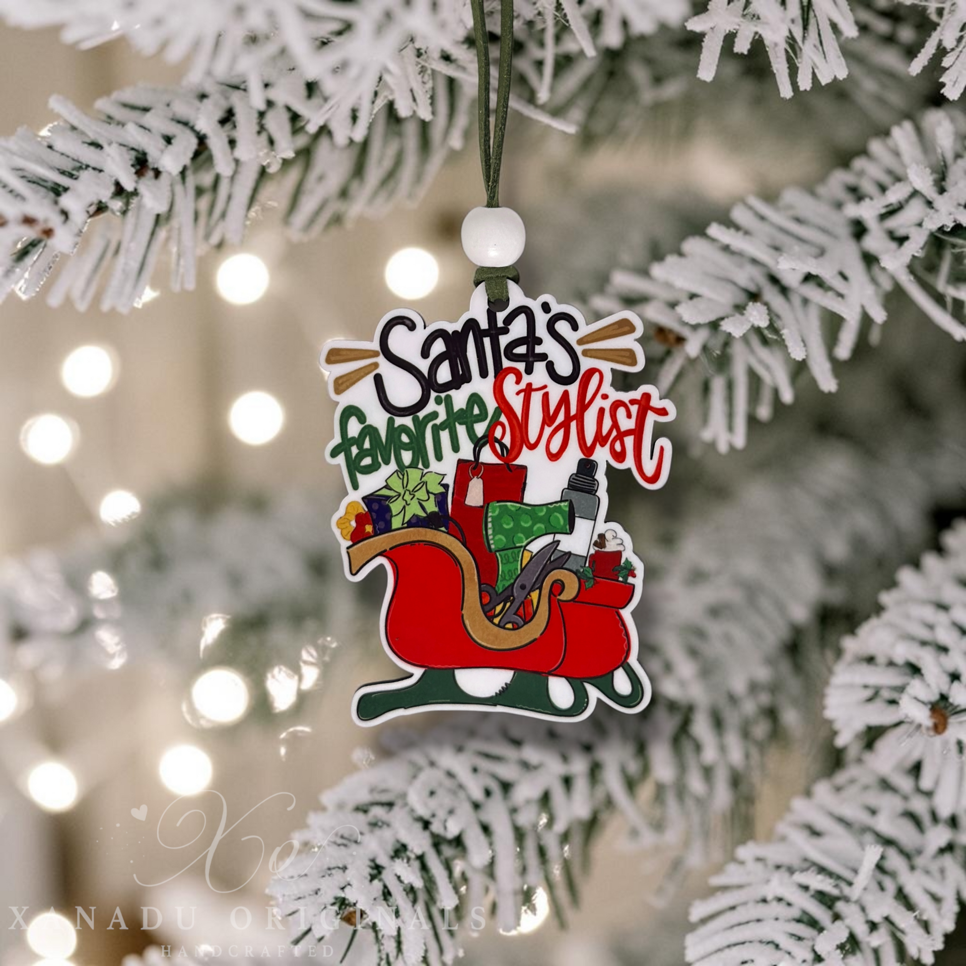 A Christmas ornament shaped like Santa's sleigh with the text 'Santa's favorite stylist' hanging from a white-frosted Christmas tree branch.