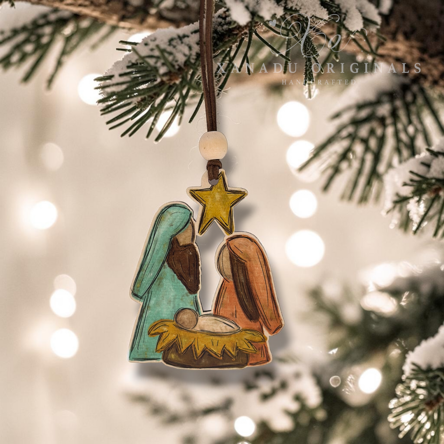 Hand-painted wooden Nativity ornament hanging from a snowy Christmas tree branch with warm bokeh lights in the background. The ornament features Mary in teal, Joseph in brown, baby Jesus in a yellow manger, and a gold star above.