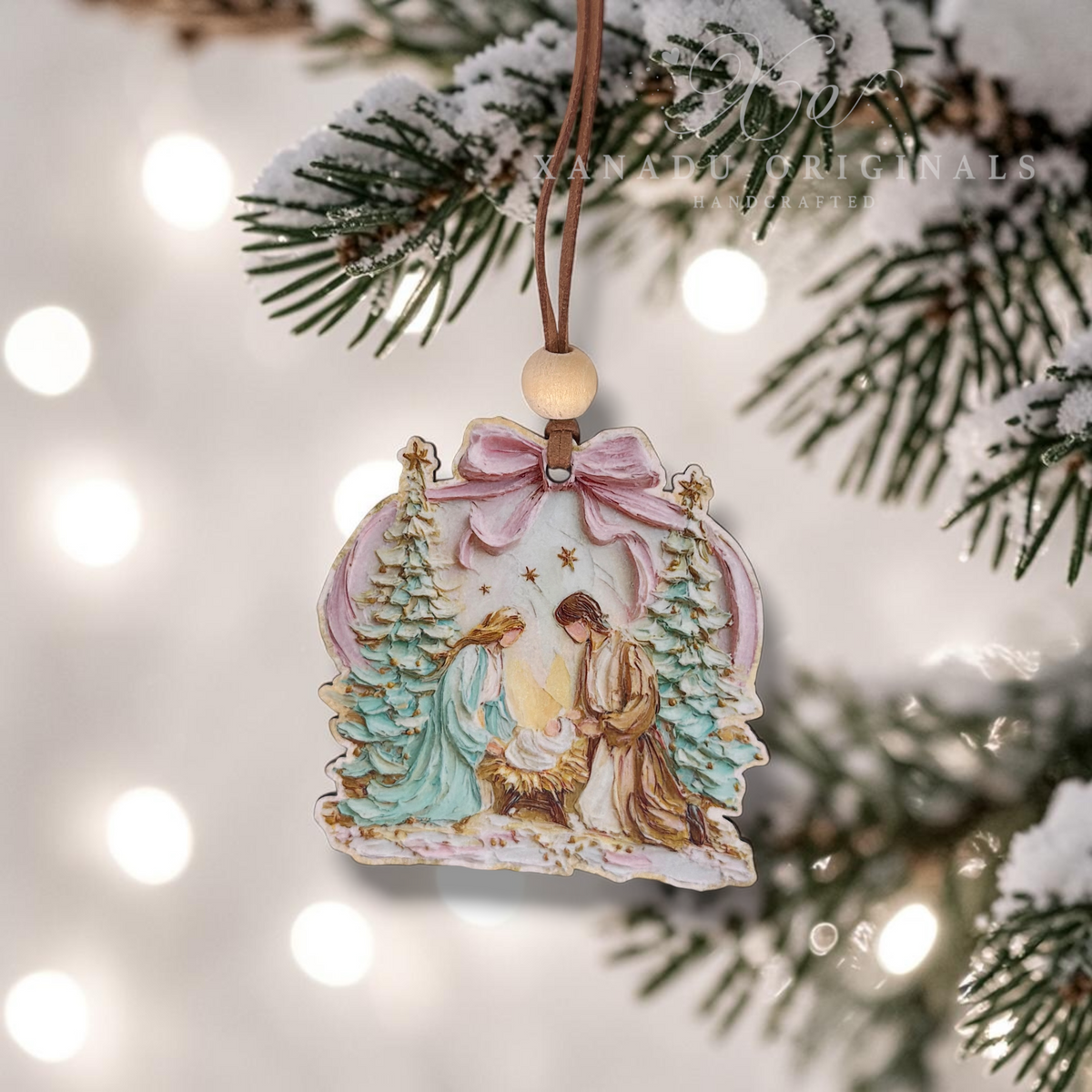A hand-painted wooden Christmas ornament depicting the Holy Family under a pink bow, hanging from a pine branch with festive bokeh lights in the background.