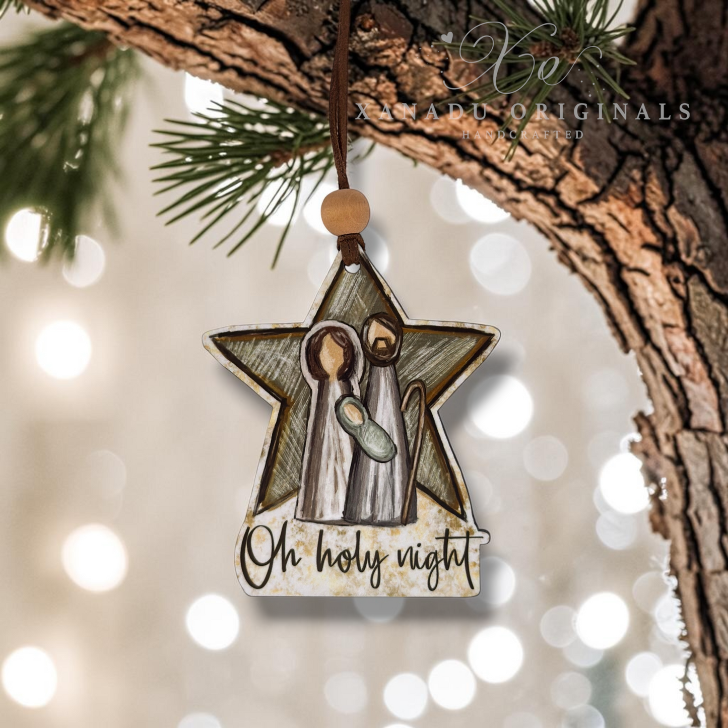 A star-shaped Christmas ornament featuring a nativity scene with the text 'Oh holy night' at the bottom, hanging from a tree branch with blurred holiday lights in the background.