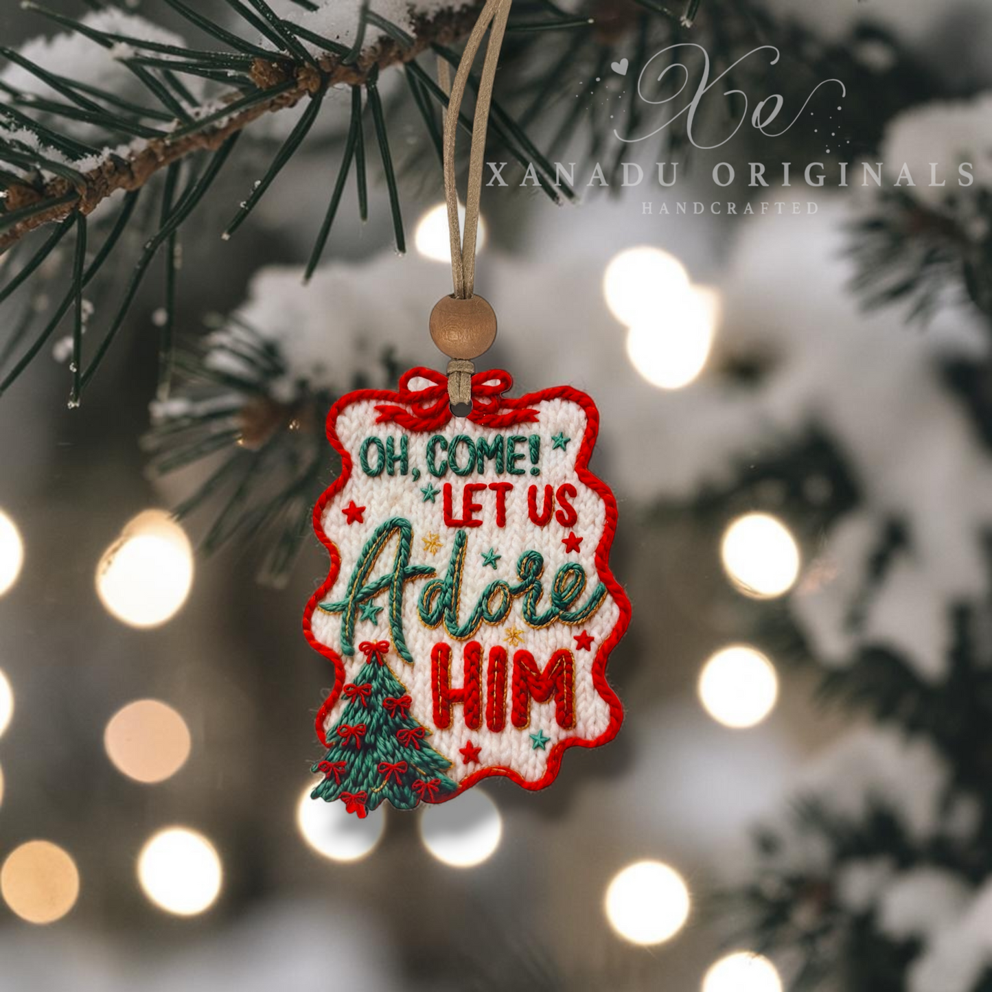 An embroidered Christmas ornament hanging from a pine branch in a snowy setting with warm bokeh lights in the background. The ornament features the text 'OH, COME! LET US Adore HIM' in green and red embroidery with a small green tree at the bottom.