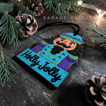 A handcrafted nutcracker ornament on a dark rustic wooden surface, surrounded by pine branches, pinecones, and warm string lights. The ornament features a colorful painted nutcracker figure and the words 'Holly Jolly' in black script on a turquoise base.