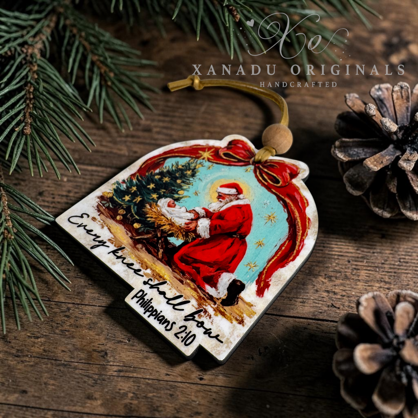 A handcrafted Christmas ornament featuring an illustration of Santa Claus with a tree and the text 'Every tree shall bow Philippians 3:21' on a rustic wooden background with pine branches and pinecones.