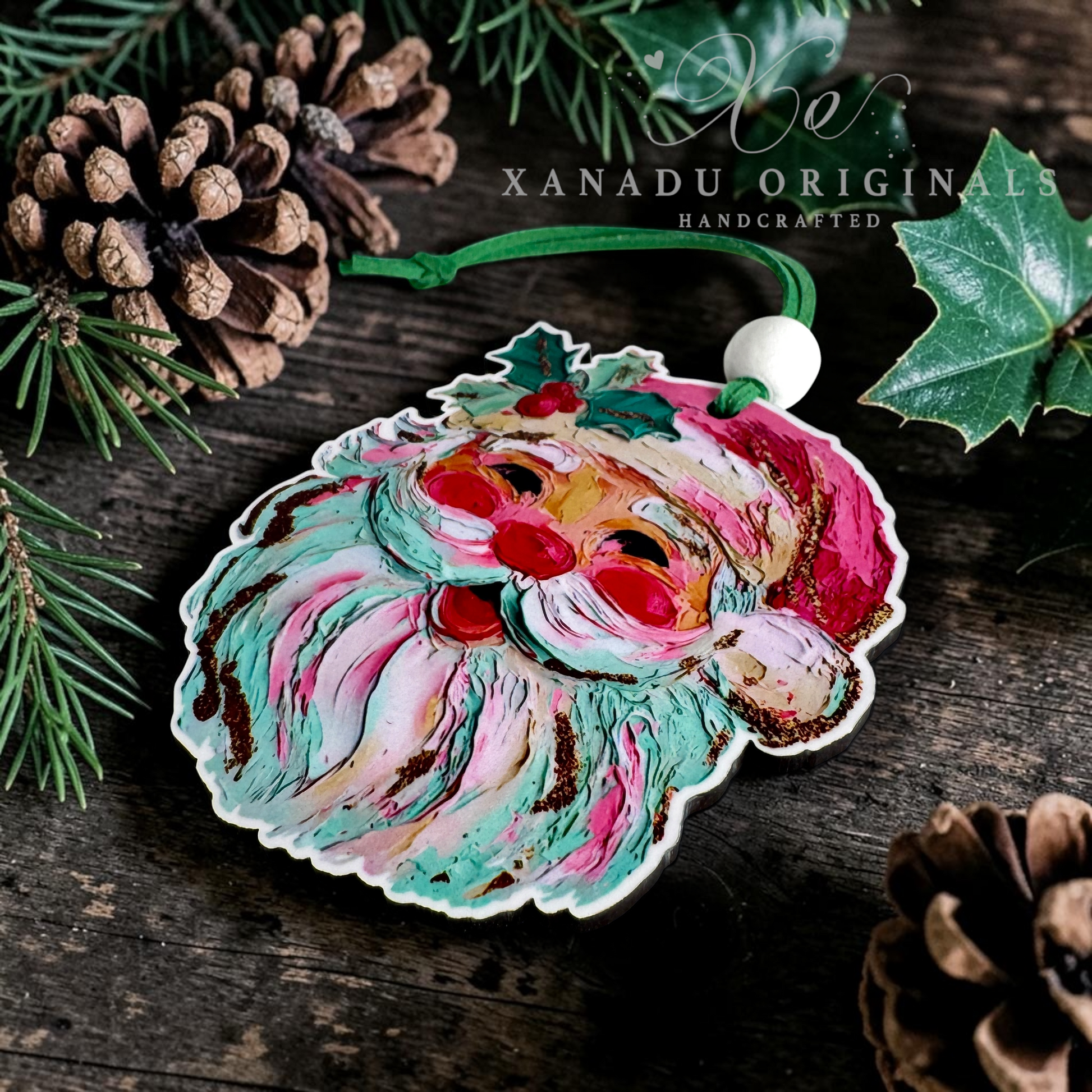 Handcrafted wooden Christmas ornament featuring a stylized Santa face with swirling teal, pink, cream, and brown painted details, hanging on a rustic dark wood surface with pinecones, evergreen branches, and holly leaves. A white bead loop and green string are visible at the top.