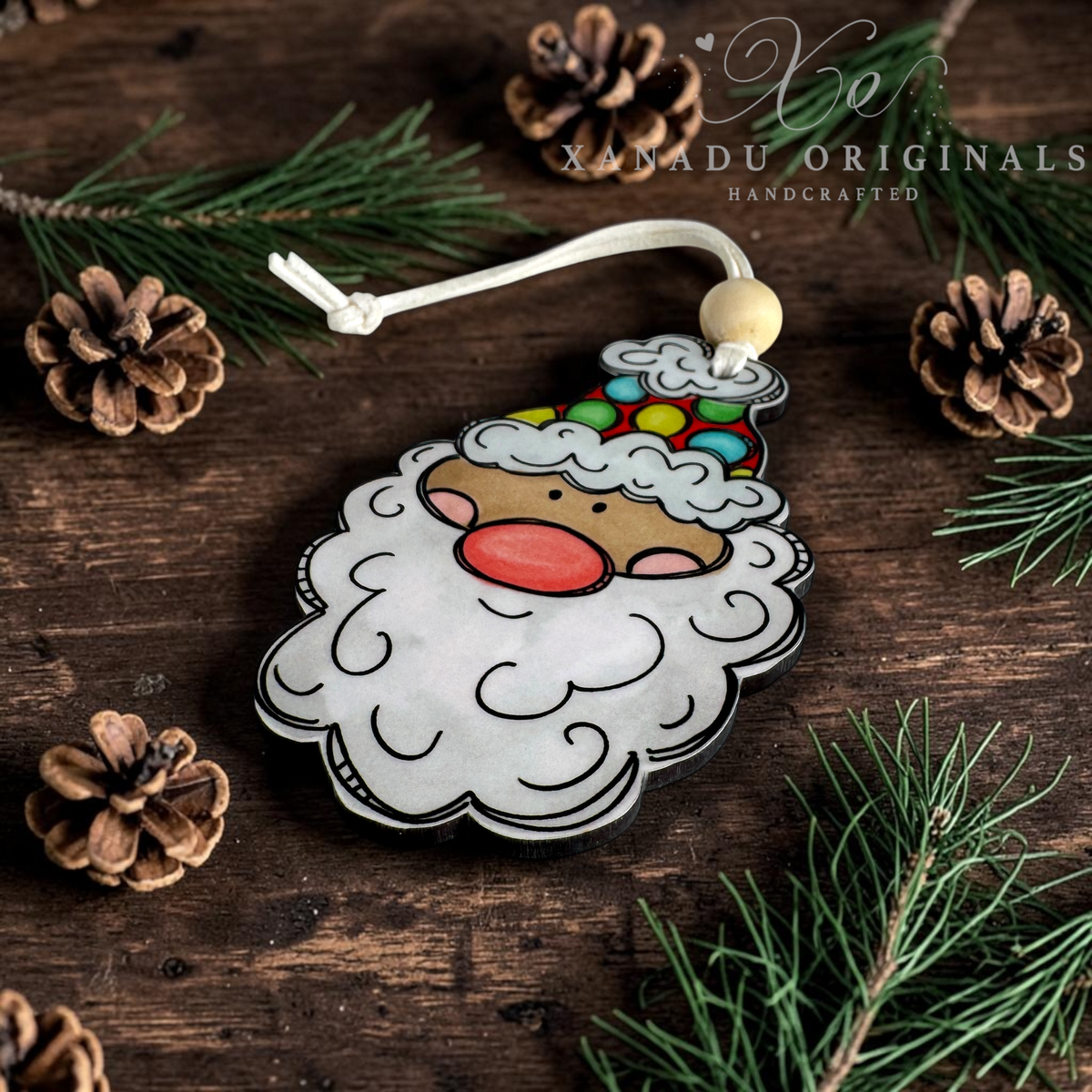 A light skin tone retro Santa face wood ornament with a bright polka dot hat and a natural wood bead, resting on a dark plank wood background with rustic pine cones.