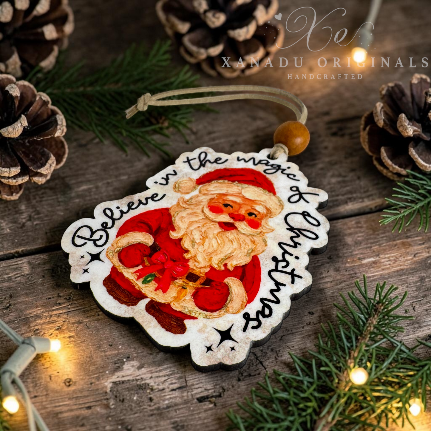 A handcrafted wooden Christmas ornament featuring an illustrated Santa Claus and the words 'Believe in the magic of Christmas,' hanging on a rustic wooden surface with pinecones, evergreen branches, and warm string lights.