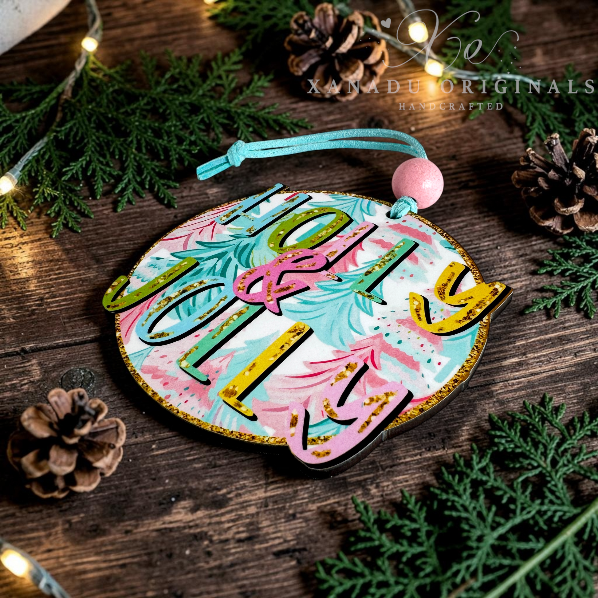 A round MDF Unisub Christmas ornament with 'HOLY & JOLLY' in gold 3D letters over a pink, teal, and white marbled background, decorated with pinecones, evergreen branches, and warm fairy lights.
